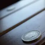 Close-up of a silver coin resting on a dark wooden surface, foreground in focus and background blurred.