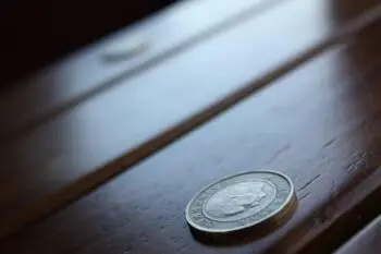 Close-up of a silver coin resting on a dark wooden surface, foreground in focus and background blurred.