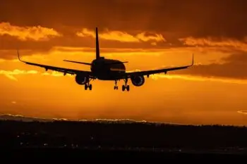 Silhouette of a passenger jet with landing gear down, approaching a runway at sunset.