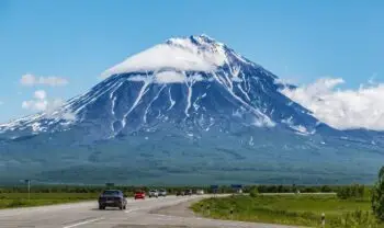 Snow-capped mountain rising above a highway with cars, under a clear blue sky.