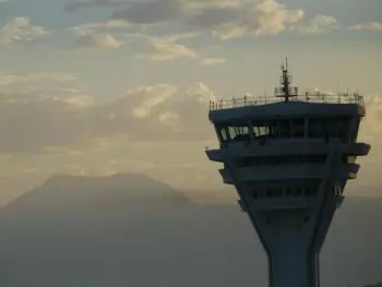 Air traffic control tower on the right with a hazy mountain range and cloudy sky in the background at sunset.